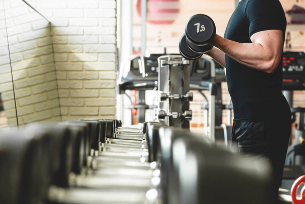 Athletic man is training with dumbbells in the gym in front of a mirror - Fotoğraf, Görsel
