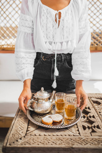 Női kezek ezüst tálcával, hagyományos marokkói menta teával, sütikkel és retro teáskannával. Vendéglátás és szolgáltatás Marokkóban. - Fotó, kép