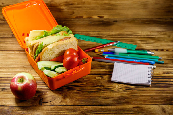 Vissza a tantervhez. Iskolai kellékek, alma és uzsonnás doboz szendvicsekkel és friss zöldségekkel egy fa asztalon - Fotó, kép