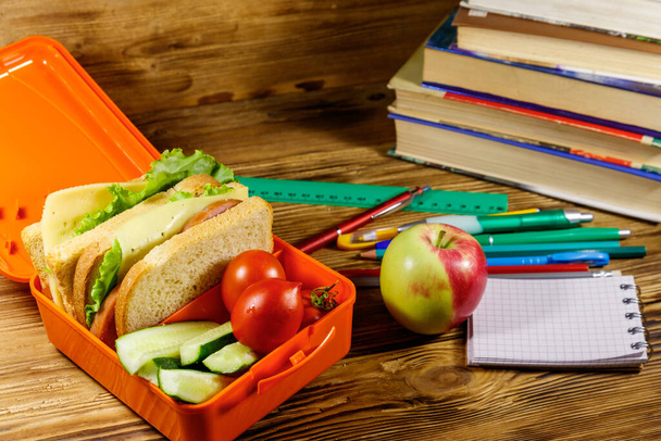 Takaisin koulunkäyntiin. Koulutarvikkeet, kirjat, omena ja lounas laatikko voileipiä ja tuoreita vihanneksia puupöydällä - Valokuva, kuva