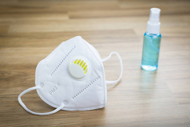 Medizinische Gesichtsmaske und Alkoholspray zum Schutz der Atemwege vor Luftverschmutzung und antimikrobielle mit Holztisch als Hintergrund. Gesundheitskonzept und Covid-19-Konzept. - Foto, Bild