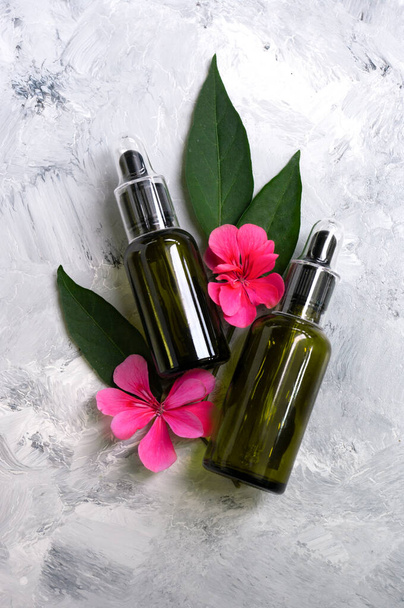 two green glass bottles with droppers. Leaves and flowers background.Copy space for text. Natural care. Cosmetic oil. - Photo, Image