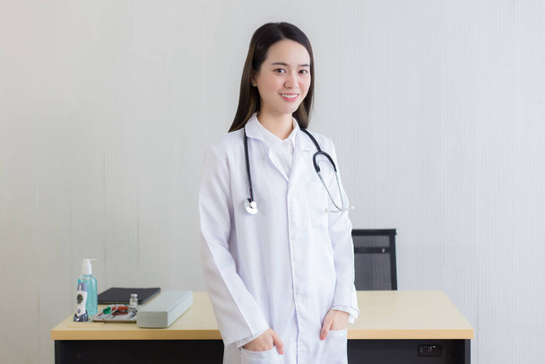  Una doctora asiática con una bata blanca de laboratorio de pie y con una bata blanca y estetoscopio. - Foto, imagen
