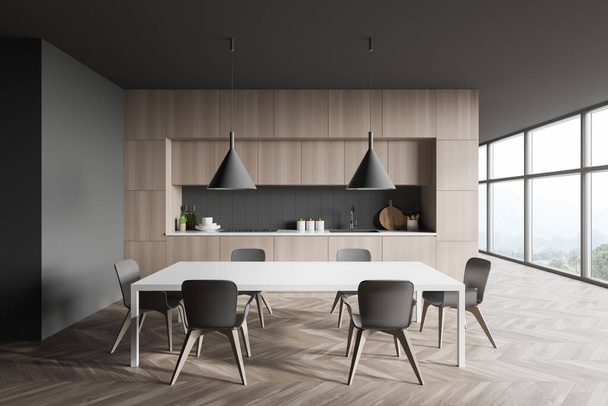 Interior of stylish kitchen with gray walls, wooden floor, wooden countertops and cupboards, dining table with chairs and panoramic window with blurry mountain scenery. 3d rendering - Фото, изображение