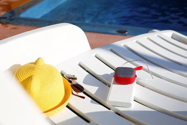 Music portable speaker is charged from the power bank via usb on a deck chair near the pool with beach accessories. Always in touch, travel gadgets, external battery for a smartphone. Place for text. Flatlay - Photo, image