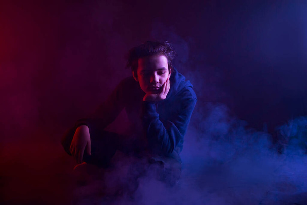Guy in thick smoke on a black background. Smoke with red and blue tint. - Фото, изображение