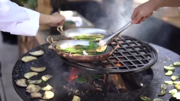 Der Koch brät die Zucchini. Gemüse vom Grill. Runder schüsselförmiger Grill mit Feuer im Inneren.  - Filmmaterial, Video
