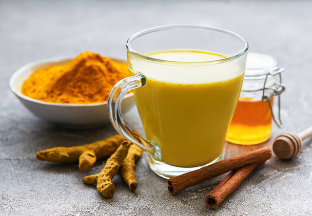Yellow turmeric latte drink. Golden milk with cinnamon, turmeric, ginger  and honey over grey concrete background. - Фото, зображення