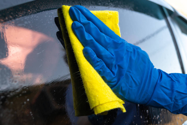 Lavado de coches, mujer en guantes azules frota vidrio auto
 - Foto, Imagen