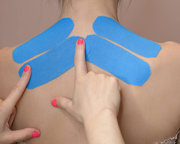 Young woman wearing blue and pink kinesio therapy tape on her shoulder. Photo - Photo, Image