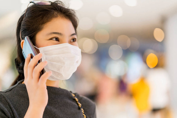 new normal after covid19 epidemic smart asian female wear protection mask hand use smartphone communication in department store new lifestyle abstract blur background - Foto, Imagen