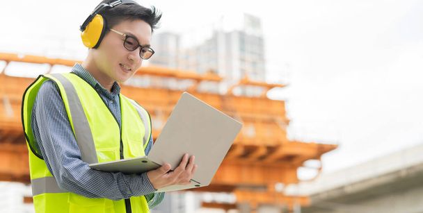 smart asian male professional civil engineer hand hold laptop site construction check with infastrcture and building background - Fotografie, Obrázek