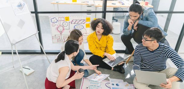 Creative asian team working on new startup project sitting on floor.Asian Business colleague brainstorm share ideas on paper chart with cheerful and enthusiasm successful business teamwork concept - 写真・画像