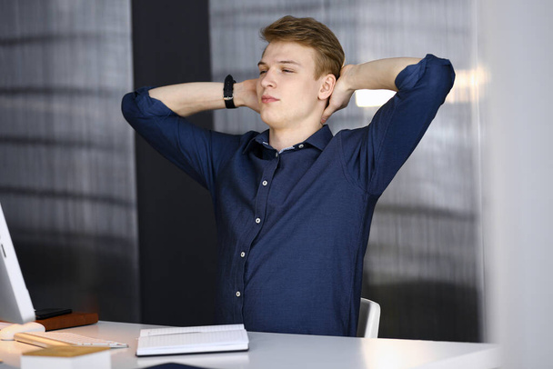 Young blond businessman and programmer stretching hands after working hard with computer. Startup business leads to success - Fotoğraf, Görsel