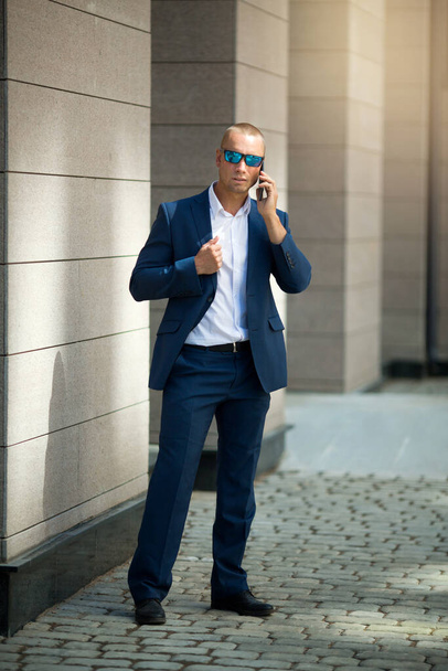 handsome young man in a summer suit on a walk in sunglasses with a phone in his hand - Foto, afbeelding