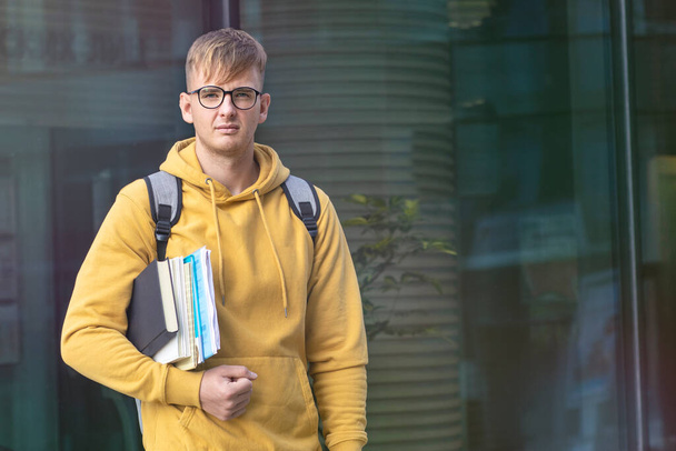 Handsome tired frustrated sad unhappy university or college student with books and textbooks in glasses with backpack. Upset serious guy standing outdoors. Overworked, study, school, education concept - Photo, Image