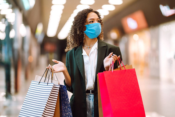 Junge Frau mit Schutzmaske gegen Coronavirus nach einem Einkauf im Einkaufszentrum. Einkäufe, Einkaufen, Lifestylekonzept. Covid-2019. - Foto, Bild