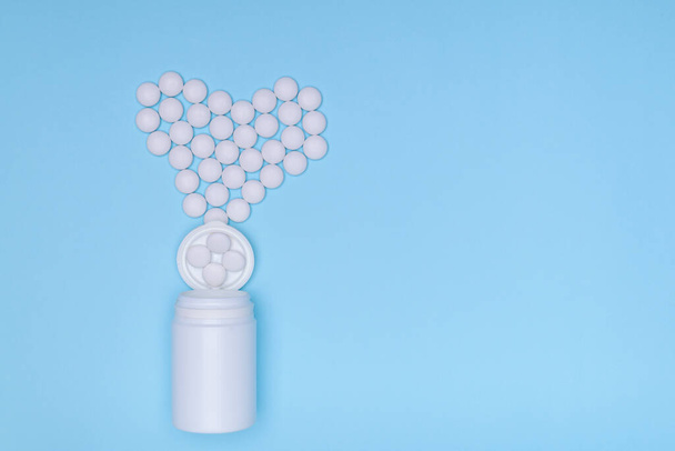 Las píldoras se presentan en forma de corazones de un frasco de pastillas sobre un fondo azul, vista superior.Píldoras botella de forma geométrica. El concepto de salud, tratamiento, elección, estilo de vida saludable. Copiar espacio
 - Foto, Imagen