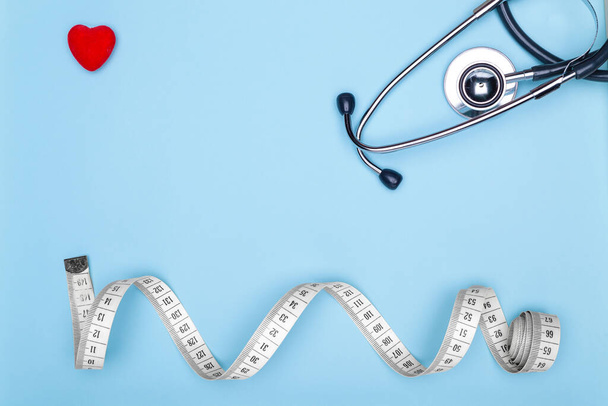 Concept of healthy lifestyle.Flexible meter, statoscope and red heart on blue background-concept of sports and fitness.Closeup of a red heart, mya meter and stethoscope on blue background. - Valokuva, kuva