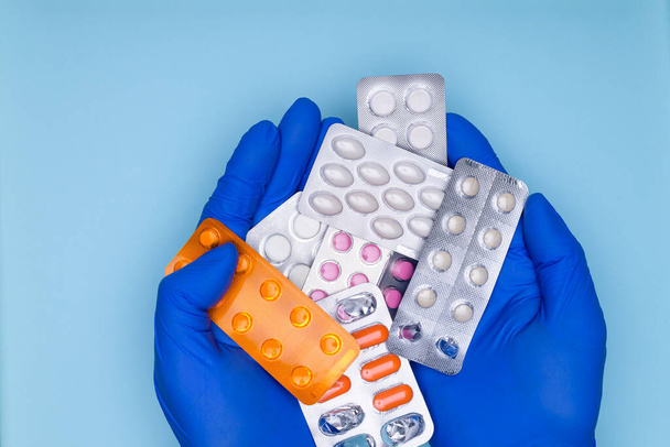 Hands of the doctor in blue gloves, holding medication in his palms, on blue background. Medication for the treatment of the disease. Drug treatment concept. - Photo, image
