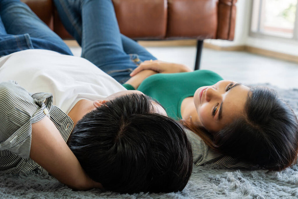 Happy Asian couple lying together on carpet at living room floor. Love relationship and lifestyle concept. - Фото, изображение