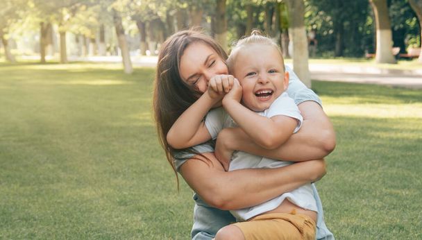 Happy young mother plays with her baby son on a sunny warm summer day in the park on the lawn. Close-up. Emotion is joy. Happy family concept - Photo, image