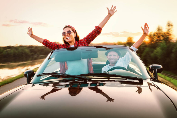 Traveling by car - happy couple in love go by cabriolet car in sunset time - Photo, image