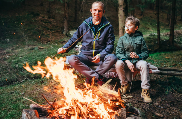Father and son roast marshmallow candies on campfire in forest - Foto, immagini