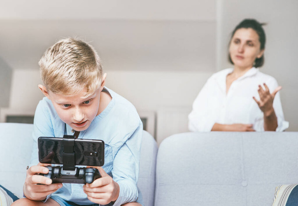 Mother unhappy with teenager son who spent his free time with electronic devices and games. Relationships teenager vs parents concept image. - Foto, Imagen