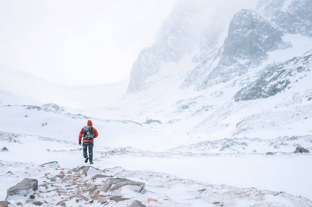 Climber walks alone in high mountains at windy snowy weather - Foto, Imagen