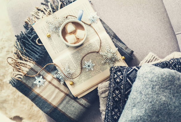 Cozy warm sweaters, plaid and cup of hot chocolate are on sofa in living room - Foto, Imagem