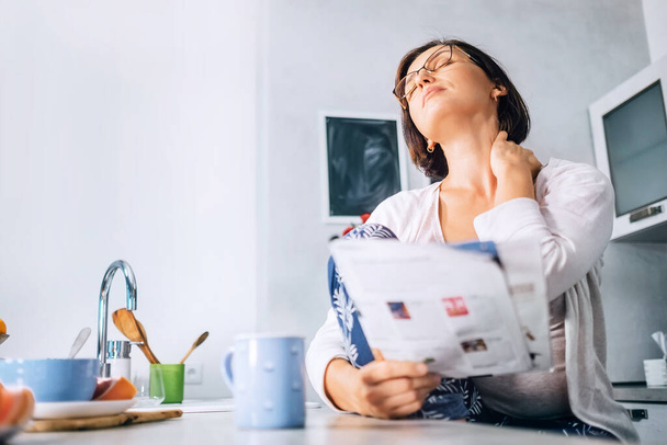 Woman has a neck pain when reads a magazine on the kitchen at morning time - Φωτογραφία, εικόνα
