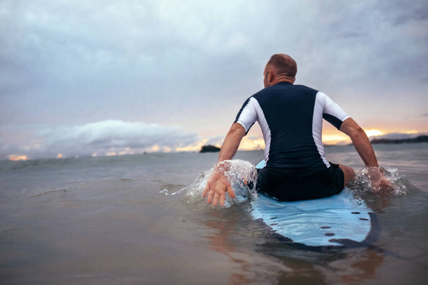 Surfer sits on surfboard on the waves in sunset time - Fotografie, Obrázek