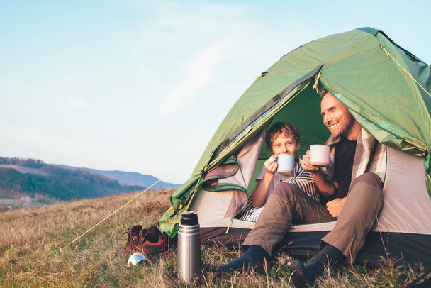 Family lisure concept image. Father and son drink a tea sitting in touristic tent - Fotografie, Obrázek
