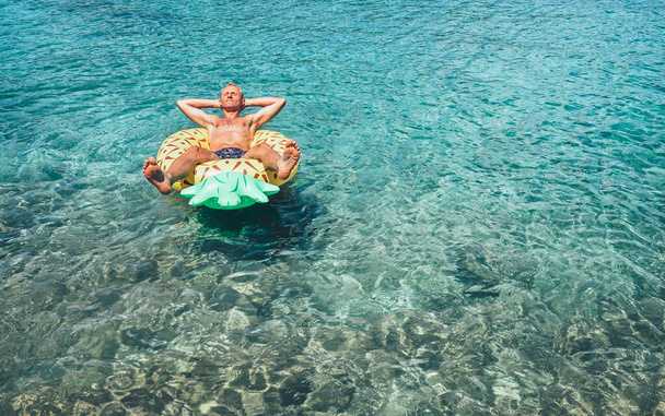 Man has relax time when swims on inflatable pineapple pool ring in crystal clear sea water - Foto, Imagem