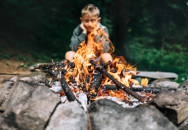 Boy sits near campfire in forest - Foto, afbeelding