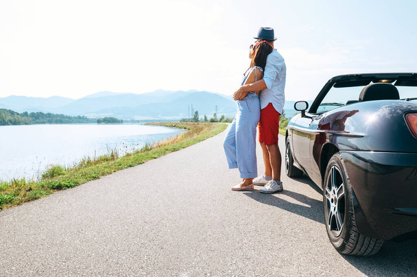 Couple in love stands near the cabriolet car on the picturesque mountain road - Foto, Imagen