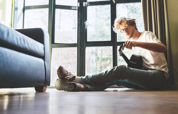 Young man sits on the floor at home and tunes the guitar - Foto, Bild