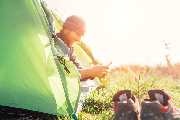 Man traveler use his mobile phone sitting in camping tent in wild nature - Foto, Imagen