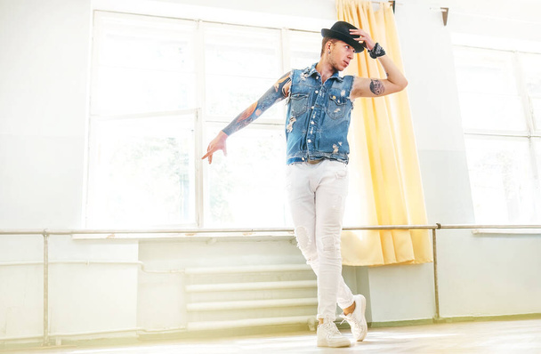 Modern tattooed art dancer teenager dressed in jeans vest, white pants and black hat dancing and mirror posing portrait - Foto, imagen