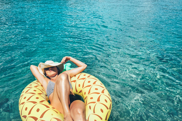 Woman swims on inflatable pineapple pool ring in crystal clear sea lagoon - Fotoğraf, Görsel
