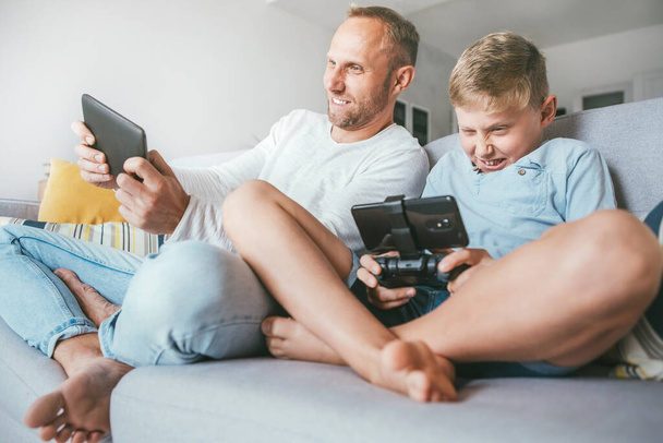 Father and preteen son playing together PC games on electronic devices - Фото, зображення