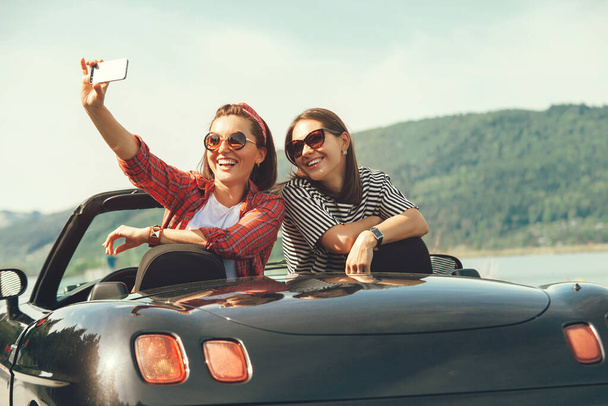 Two female friends take a selfie photo in cabriolrt car during their summer voyage - Valokuva, kuva