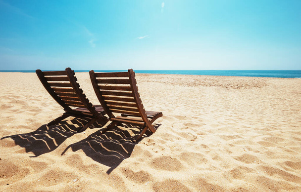 Two beach chairs on empty ocean beach under bright shining sun - 写真・画像