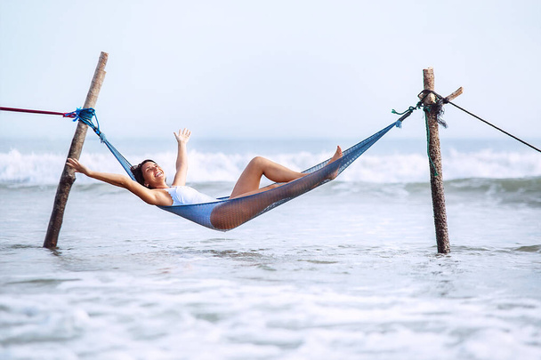 Happy smiling woman lies in hammock swing over the ocean surf line - Fotó, kép