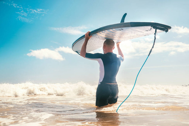 Young Man surfer with long board on head goes to the sea to have a surf practice. Learning surfing concept. - Foto, Imagen