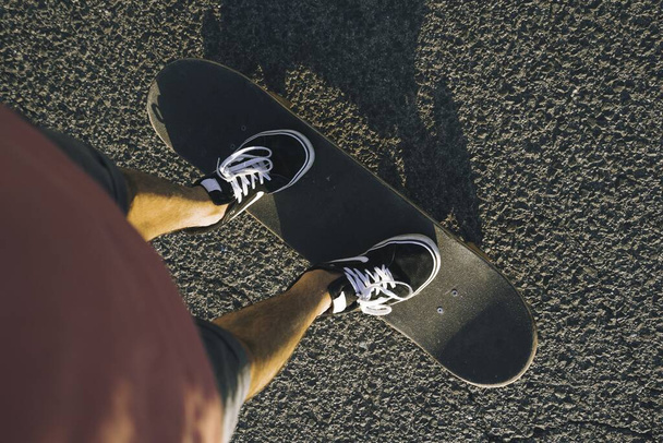Um tiro de ângulo alto das pernas de um macho montando um skate no chão de asfalto
 - Foto, Imagem