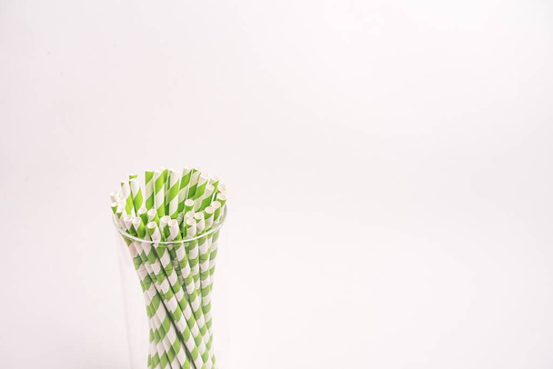A closeup shot of green and white striped drinking tubes in a glass isolated on a white background - Foto, afbeelding