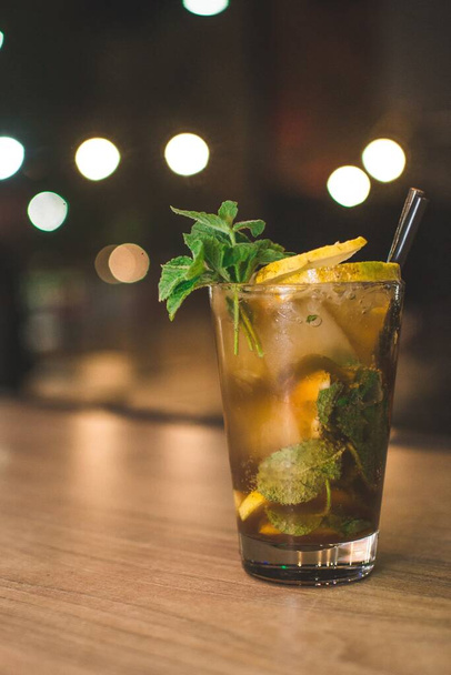 A cold beverage with ice cubes, lemon slices, mint leaves and a black straw - Photo, Image