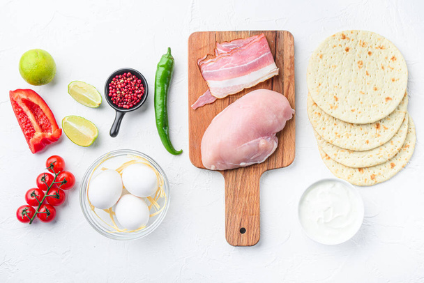 Ingrédients pour tacos de poulet, tomates, maïs, oeuf, poivre, viande de poulet au citron vert et tortillas sur fond texturé blanc vue du dessus - Photo, image